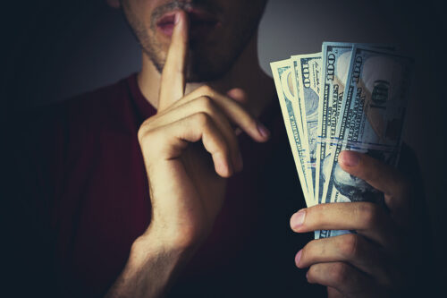 man going shhh with money implying embezzlement